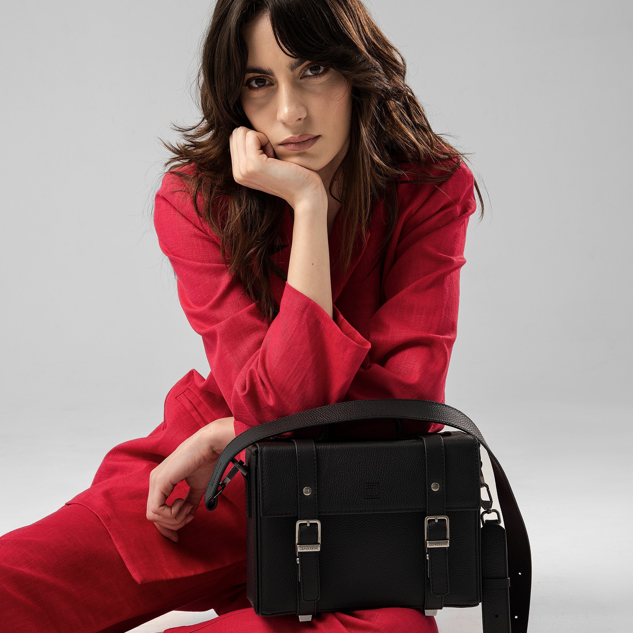 Model in red suit holding the black Dobby bag in a modern crossbody style