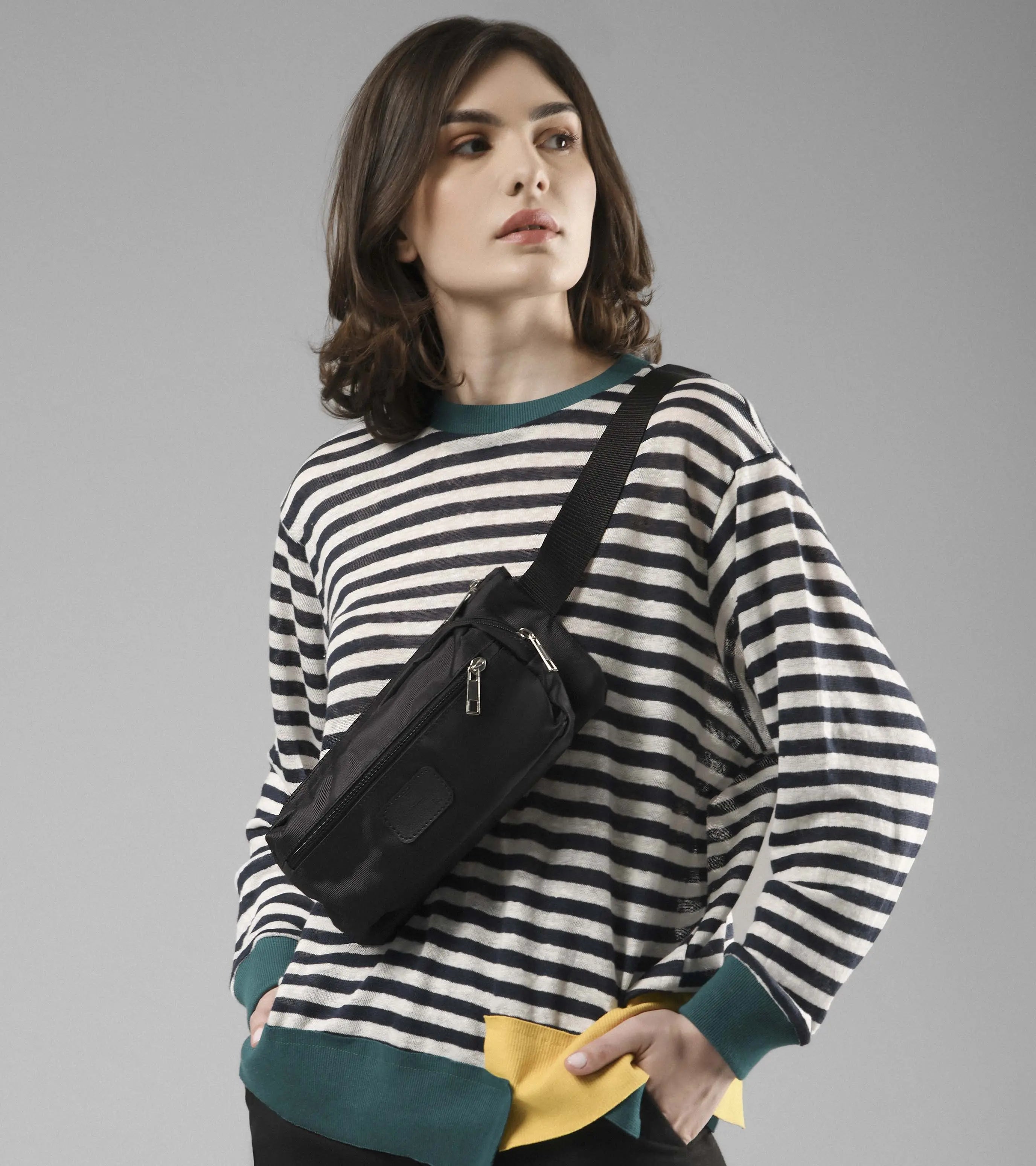 Model wearing Bellamy black belt bag crossbody over striped sweater, hands in pockets