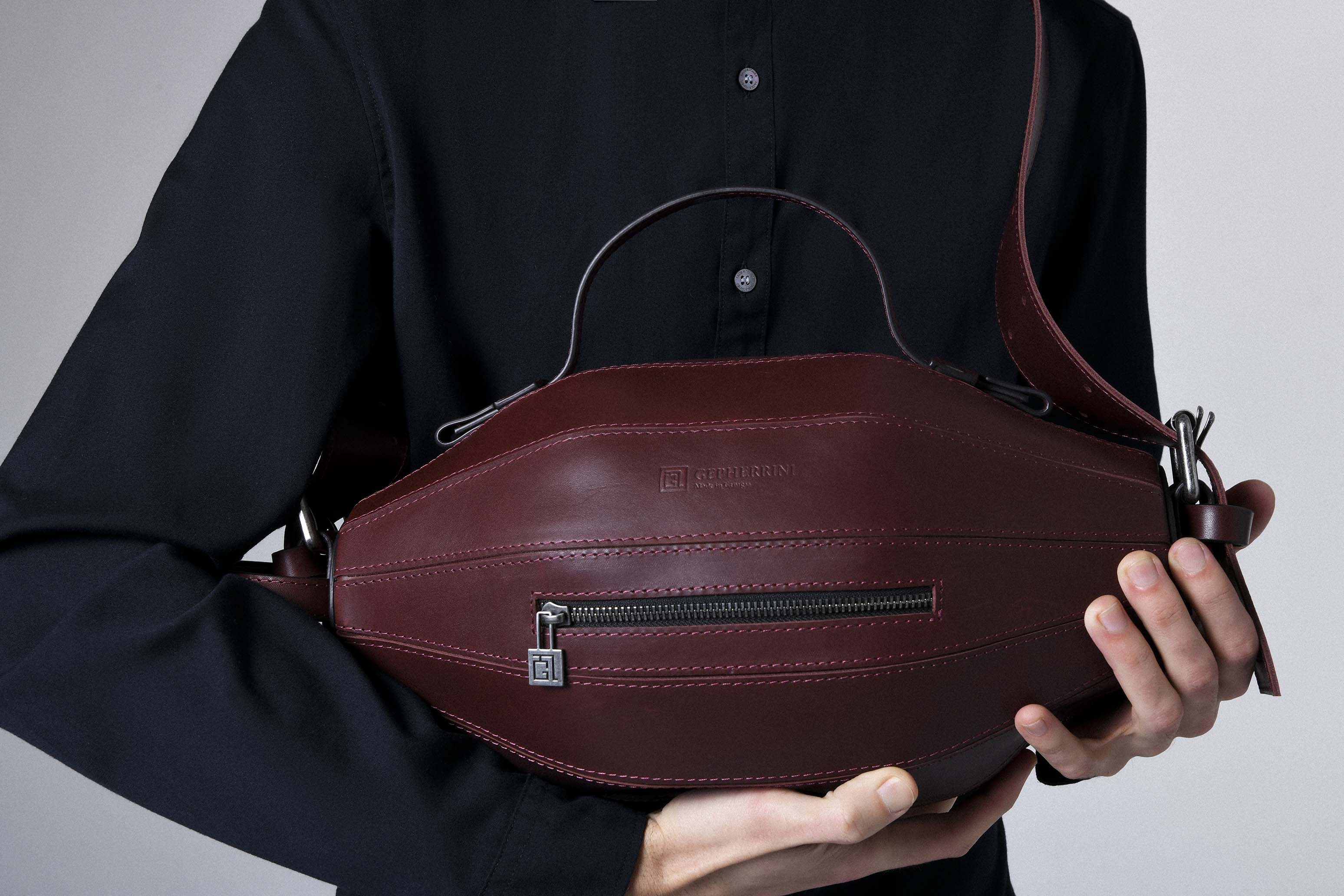Model holding the Ellisse Bag in burgundy leather, highlighting its sculptural shape and rich color.