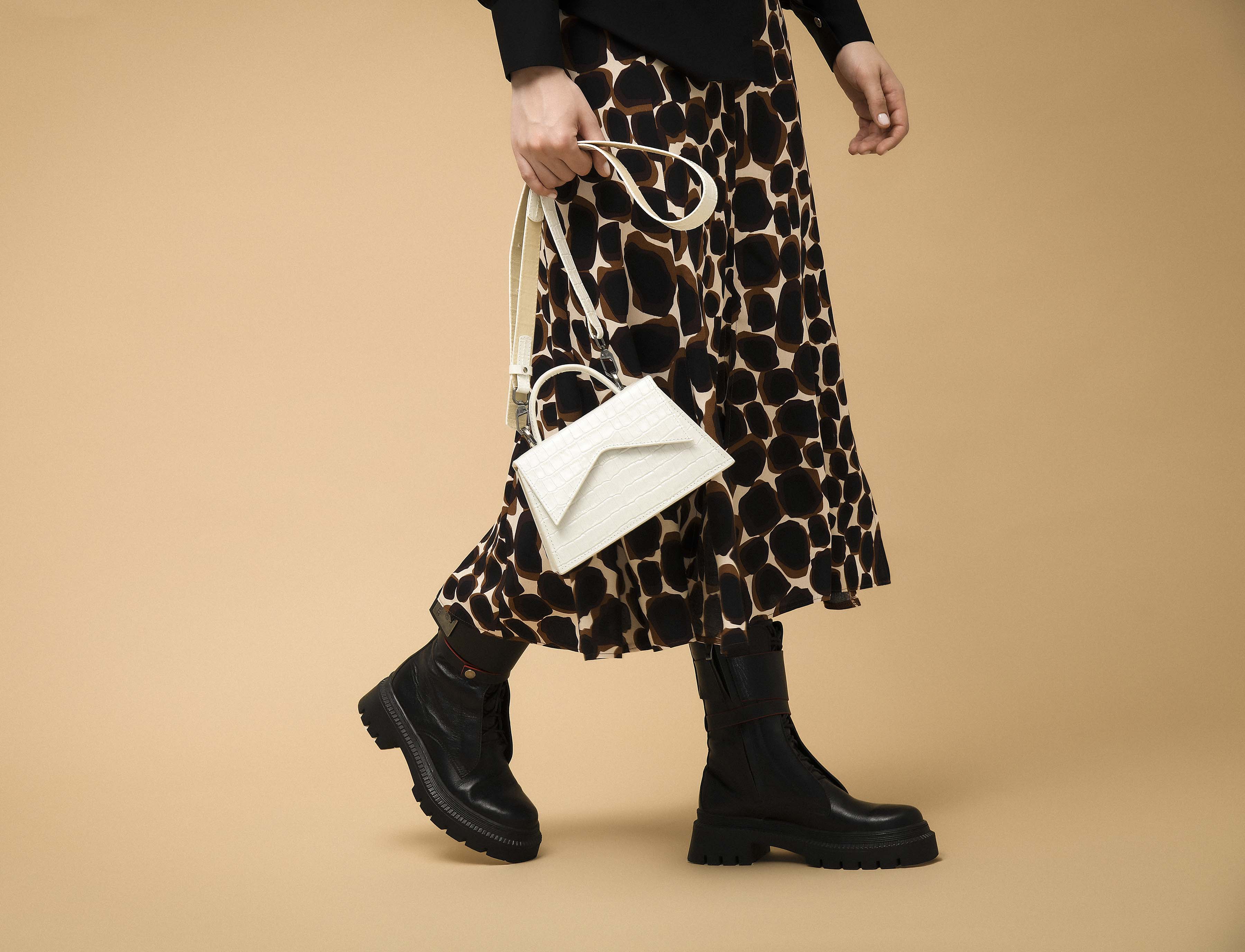 Model carrying Evelyn beige leather handbag styled with printed skirt and boots