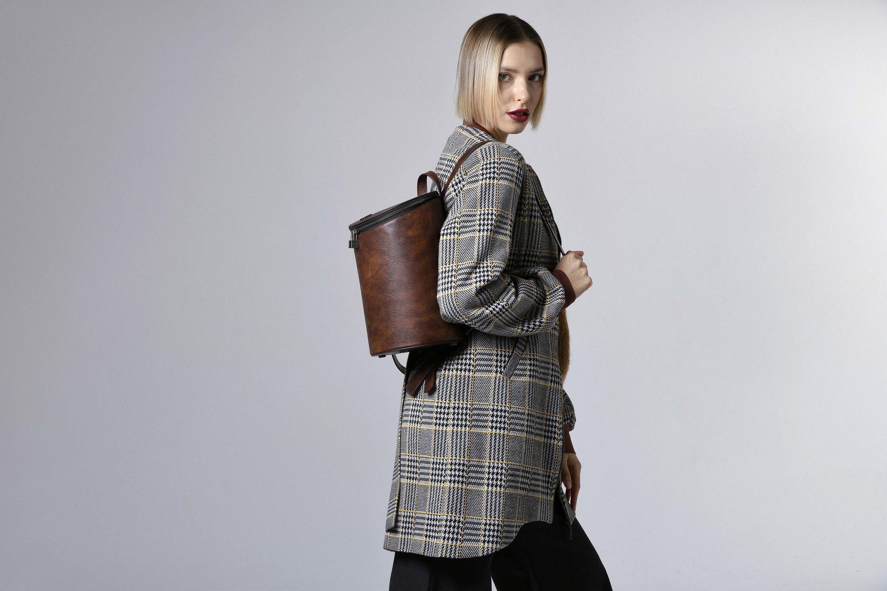 Model wearing the Frida backpack by Gepherrini – brown leather bag styled with plaid coat