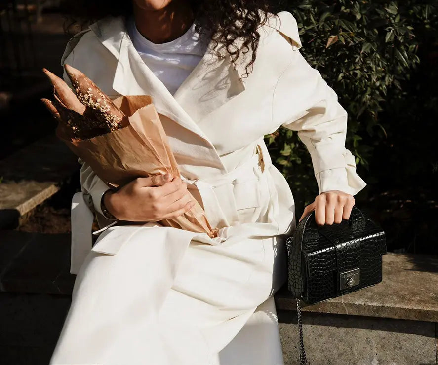 Woman in a white trench coat holding the Genesis black leather handbag with croc texture