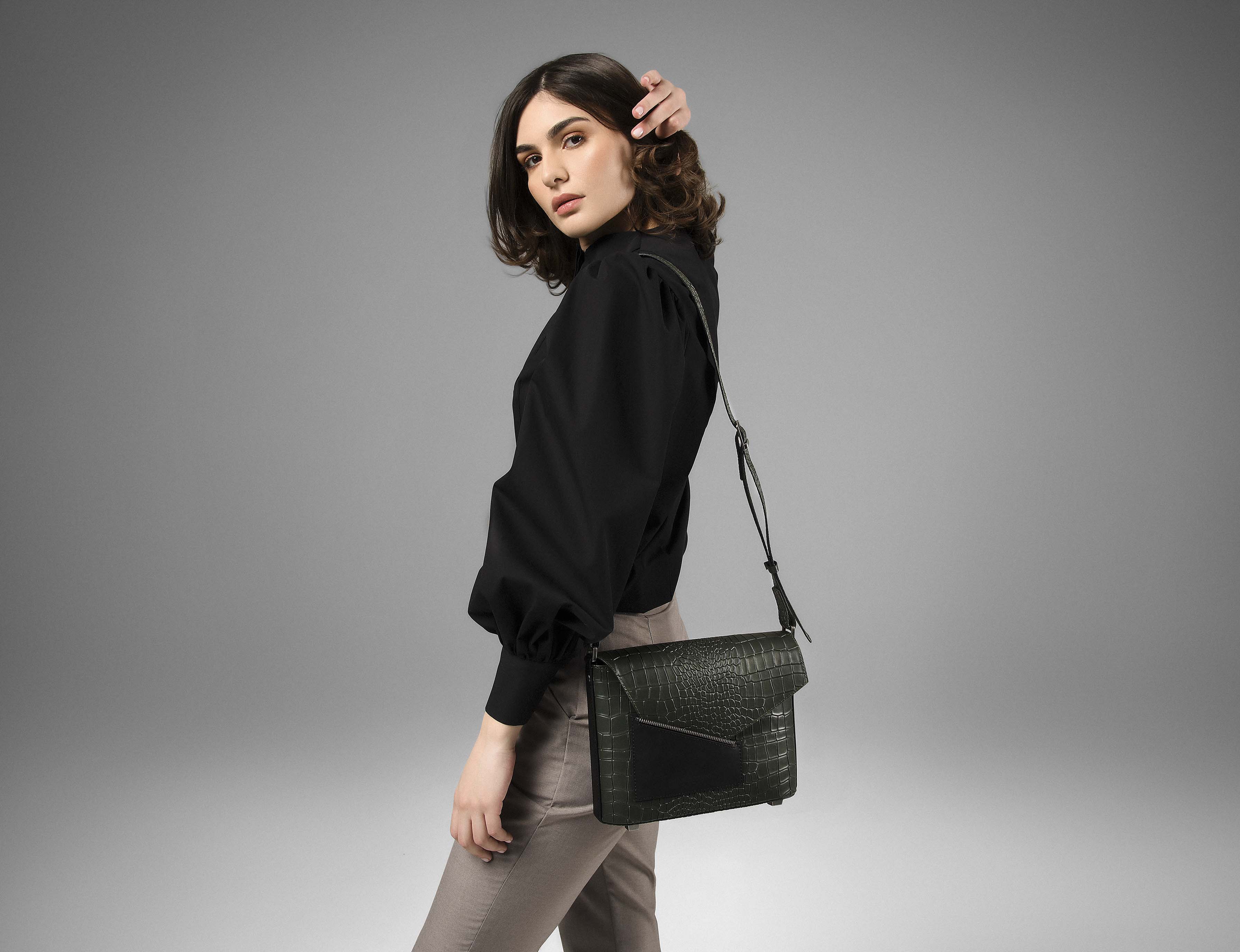 Model wearing the Lita moss green leather shoulder bag with black blouse and taupe pants.