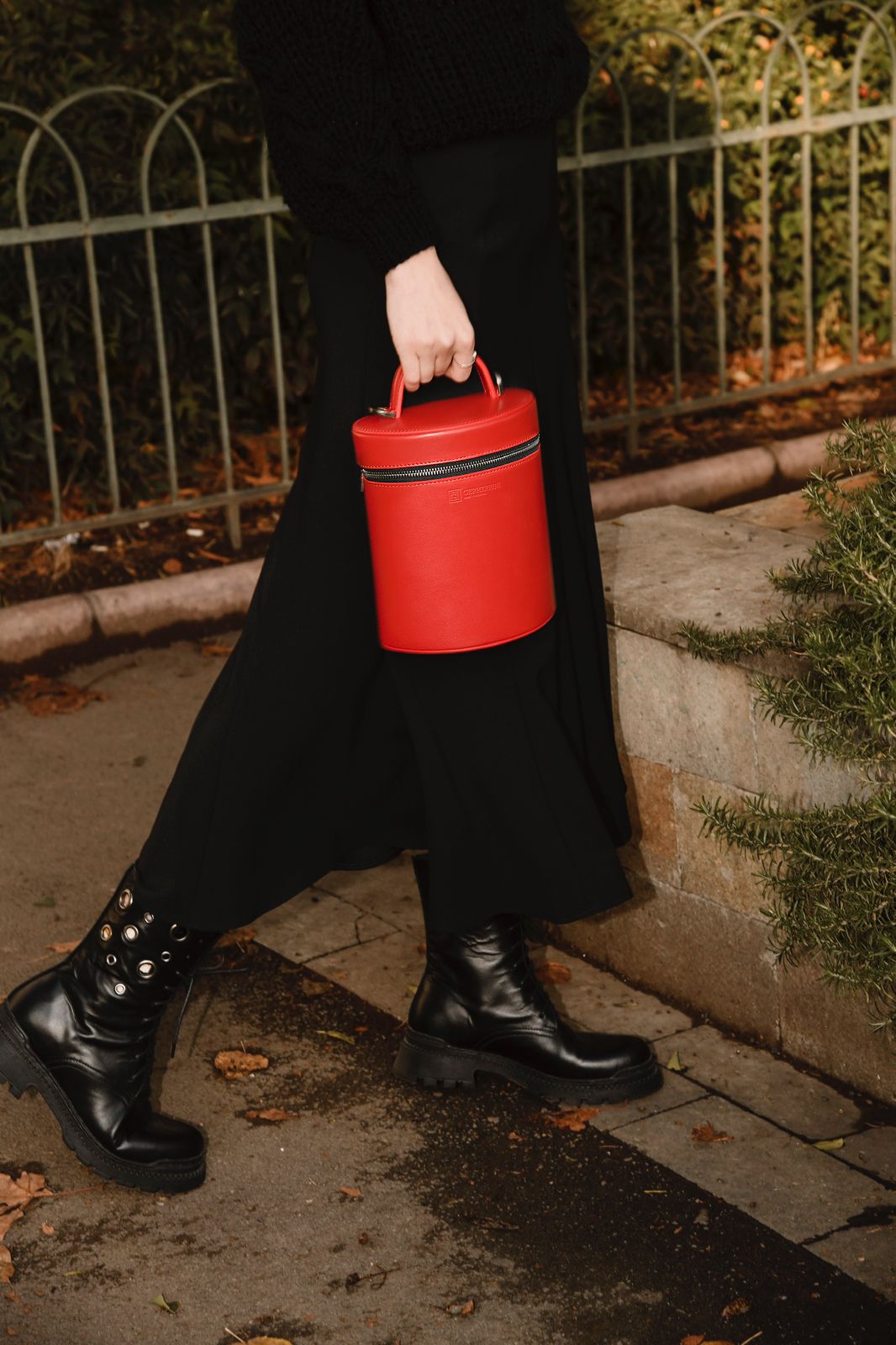 Model walking outdoors with Mia red leather handbag in hand, styled with black boots and skirt